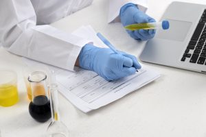 Mãos com luvas segurando uma amostra de urina e fazendo anotações para exame toxicológico